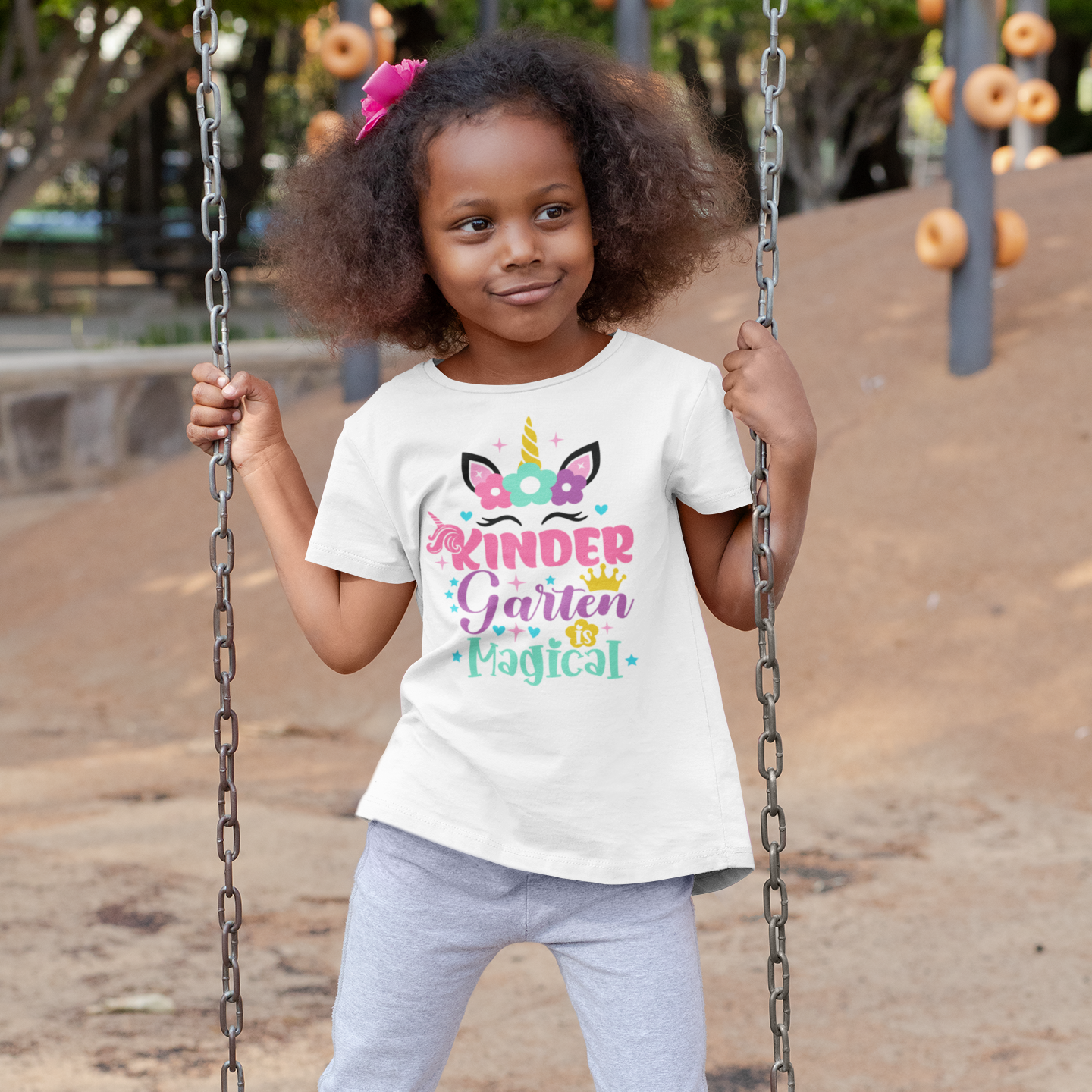 Young girl on a swing wearing a white t-shirt with colorful text and graphics.